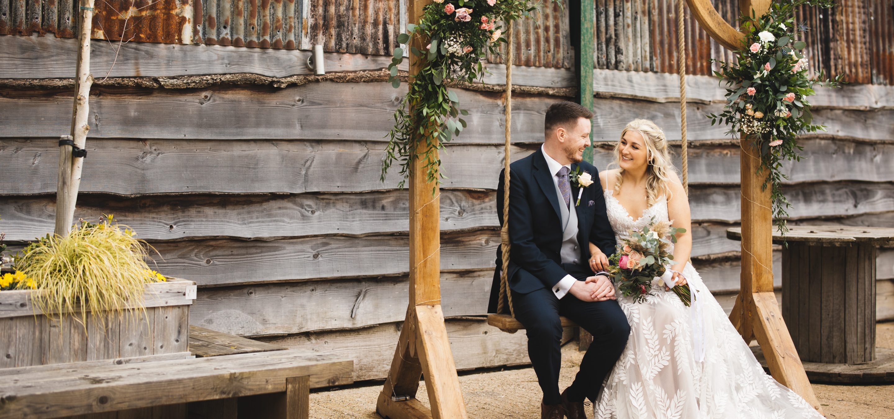 Bride and groom sat on swinging chair outside barn venue