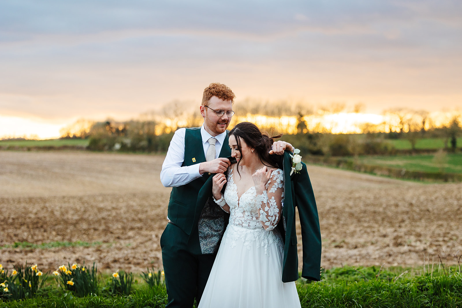 Groom putting on jacket for bride in countryside