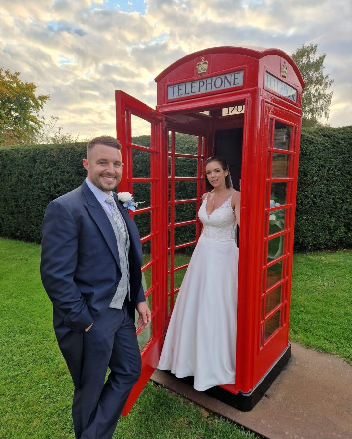 Man and woman stood next to red telephone box at barn wedding venue